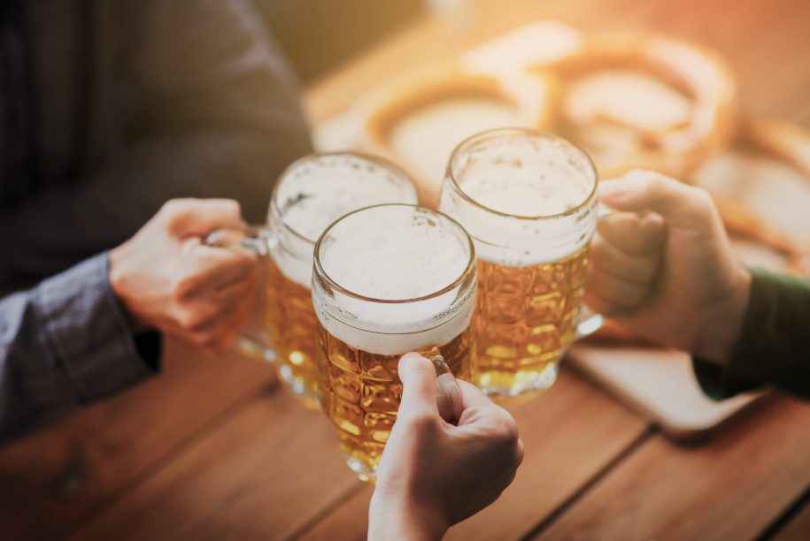 people, leisure and drinks concept - close up of hands clinking beer mugs at bar or pub